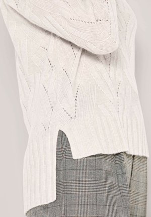 White knitted sweater with textured geometric pattern and side slit over gray plaid pants.