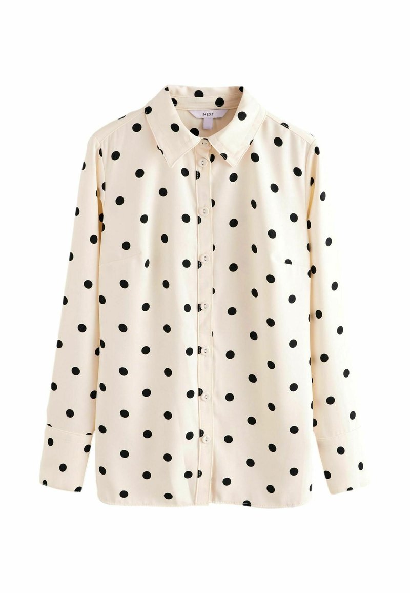 Blouse crème à manches longues à pois noirs, boutonnée devant et col en pointe, présentée sur fond blanc uni.