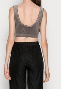 Szary, krótki top z weluru z szerokimi dziurami na ramiona i okrągłym dekoltem, połączony z czarnymi, szerszymi spodniami o fakturowanej powierzchni. Widok z tyłu pokazuje szczegóły gładkiego materiału.