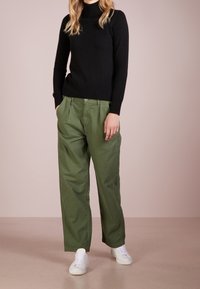 Czarny sweter z golfem i oliwkowe szerokie spodnie. Spodnie mają plisy i kieszenie; połączone z białymi sneakersami. Gładkie tekstury.