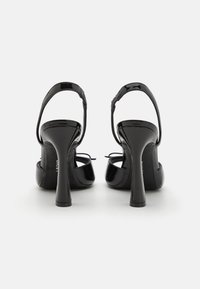 Black patent leather high-heeled sandals with a curved heel, open back, and ankle strap. Features a smooth texture and delicate lacing.