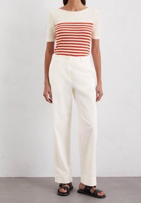 Top de manga corta con rayas horizontales rojas y blancas, combinado con pantalones anchos blancos y sandalias negras. Tejido suave con un corte relajado.