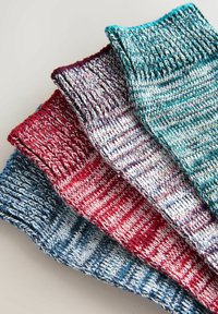 Štyri páry zložených žebrovaných pletených ponožiek v tyrkysovej, bordovej, červenej a modrej farbe usporiadaných diagonálne na svetlom podklade.
