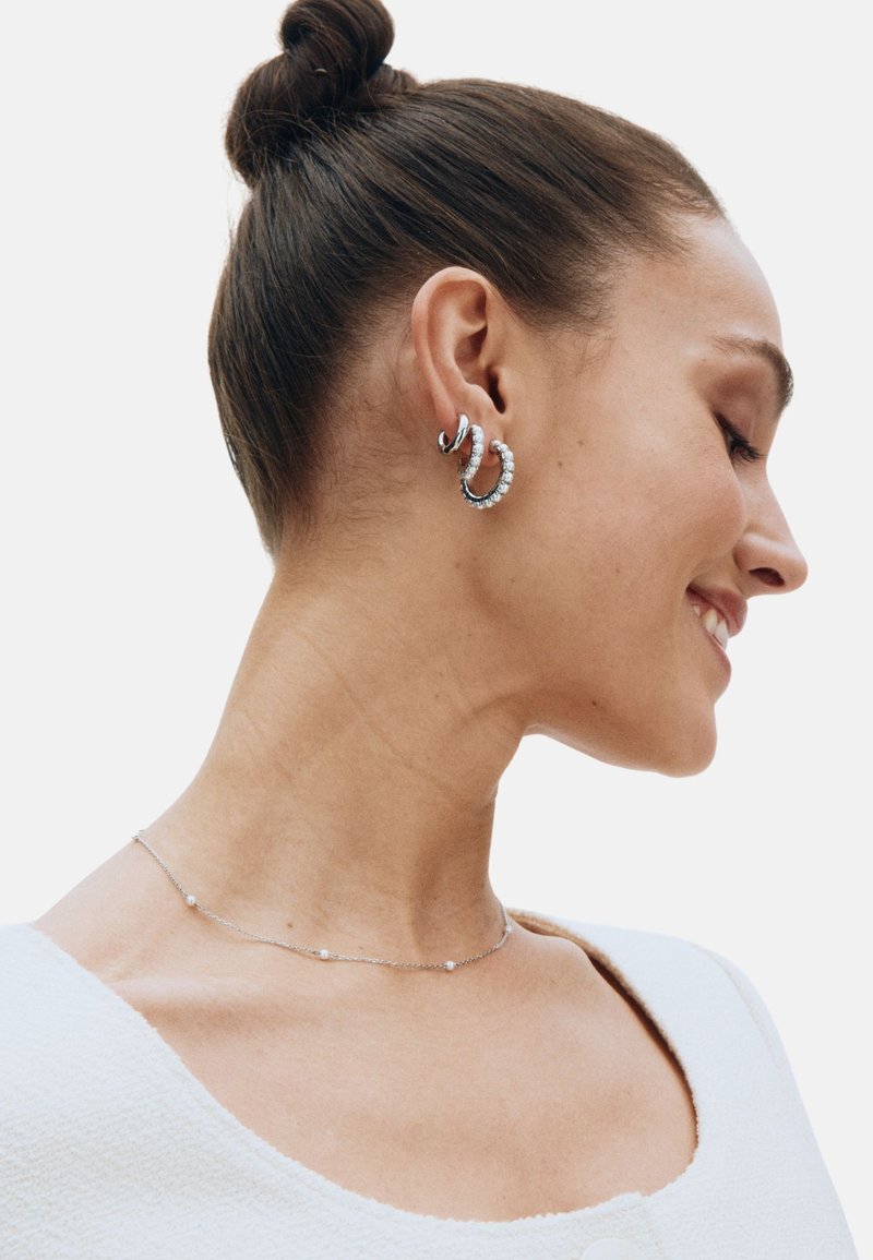 Boucles d'oreilles créoles en argent avec des motifs entrelacés ornés de petites pierres blanches. Un collier délicat en argent avec des accents circulaires espacés.