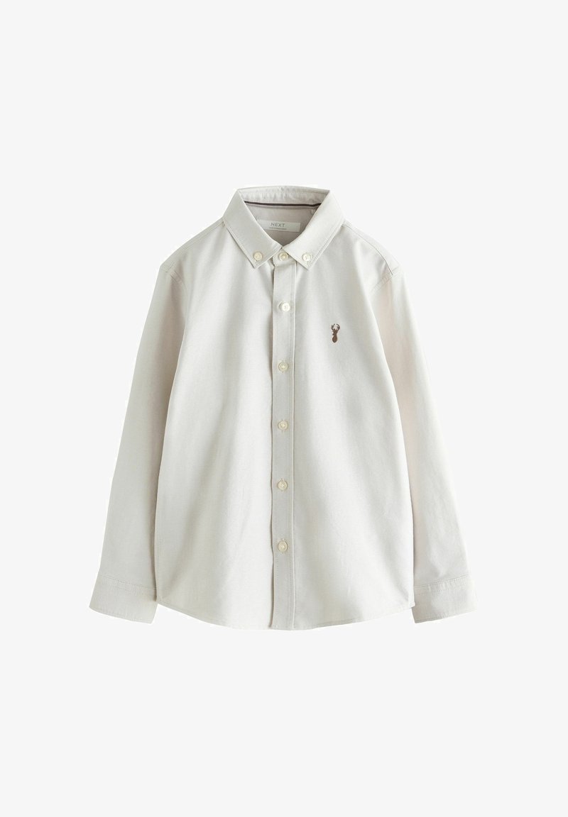 Chemise blanche à manches longues avec boutons, col et petit emblème brun en forme de cerf sur le côté gauche de la poitrine.