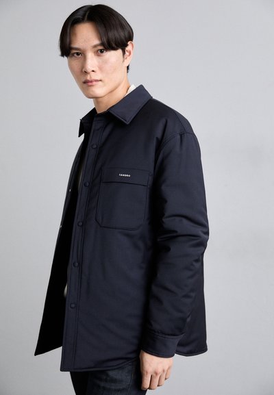 Giacca button-up di colore blu navy con colletto e taschino sul petto, con un logo sottile, realizzata in un tessuto morbido e leggero.