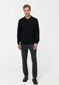 Must musta polo särk, millel on pikad varrukad ja krae, kombineeritud tumedate hallide kitsaste pükste ja mustade kingadega, valgel taustal.