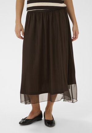 Hnedá dlhá sukňa s elastickým pásom a priehľadnou vrstvou, doplnená čiernymi plochými topánkami s mašľou.