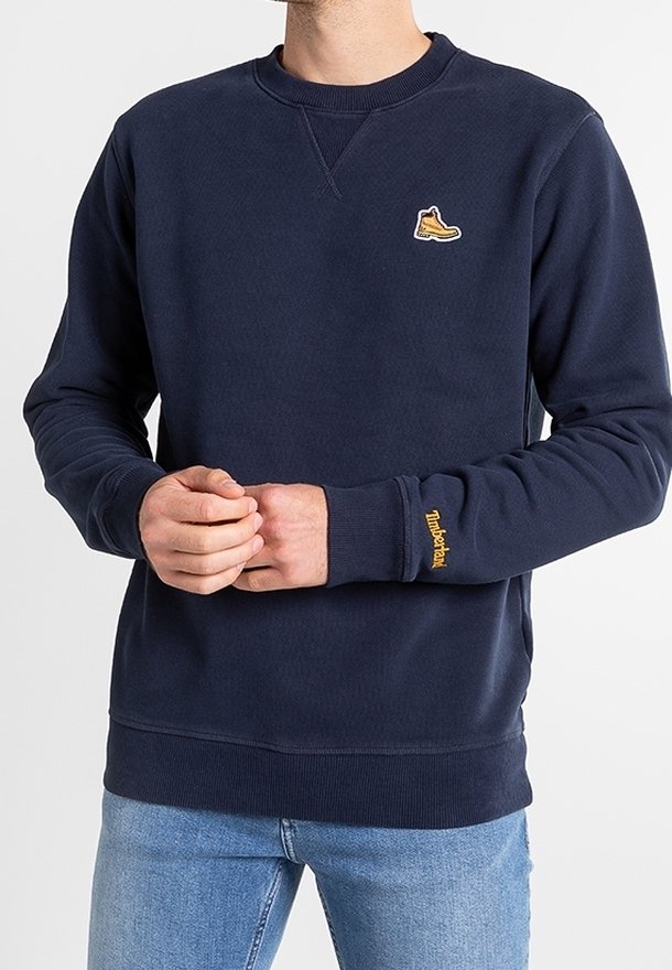 Dunkelblaues Sweatshirt mit gerippten Bündchen und Saum, ausgestattet mit einem gelben Sneaker-Patch auf der Brust und dezenten Texturdetails im Stoff.