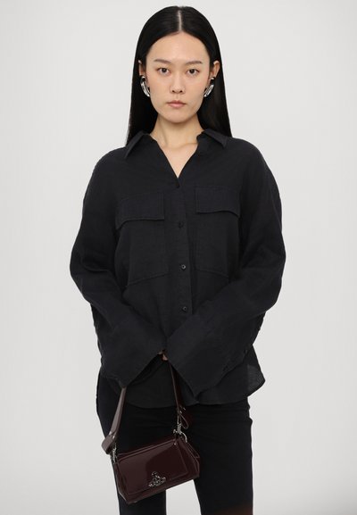 Black linen button-up shirt with two chest pockets, wide cuffs, and a relaxed fit, paired with a small burgundy leather handbag.