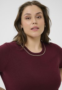 Top de punto burdeos con escote redondo adornado con una cadena de cuentas metálicas, mangas cortas y una textura suave.