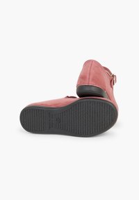 Scarpe in suede rosa con retro chiuso, cinturino regolabile e suola in gomma nera testurizzata, che mostrano un design semplice e funzionale.