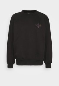 Čierna mikina so stočenými manžetami a lemom, s malým logom v purpurovej farbe. Vyrobená z mäkkého materiálu, vo voľnom strihu a s raglánovými rukávmi.