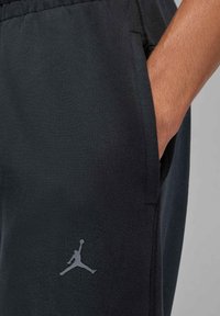 Zwarte sportbroek met een gladde textuur, voorzien van een zijzak en een grijs Jumpman-logo op het dijbeen.