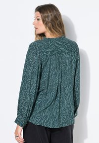 Camicia verde a maniche lunghe con un sottile motivo a zebra, in tessuto leggero, dotata di dettagli plissettati sulla scollatura e polsini con bottoni.