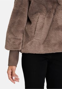 Puhány, taupe színű fleece pulóver széles ujjal és bordás mandzsettával. Oldalsó zsebbel rendelkezik és puha, meleg anyagból készült.