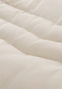 Couverture matelassée crème avec un tissu lisse et texturé, présentant des motifs de couture uniformément espacés et une apparence douce et duveteuse.