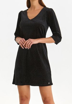 Schwarzes Kleid mit Dreiviertelärmeln, V-Ausschnitt und goldfarbenem Pünktchenmuster. Weicher Stoff, leicht ausgestellte Form, mit einem kleinen runden Akzent.