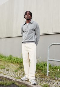 Γκρι φλις πόλο με φερμουάρ ενός τετάρτου, άσπρο λογότυπο, συνδυασμένο με κρεμ παντελόνι wide-leg και γκρι αθλητικά με ανακλαστικές λεπτομέρειες.