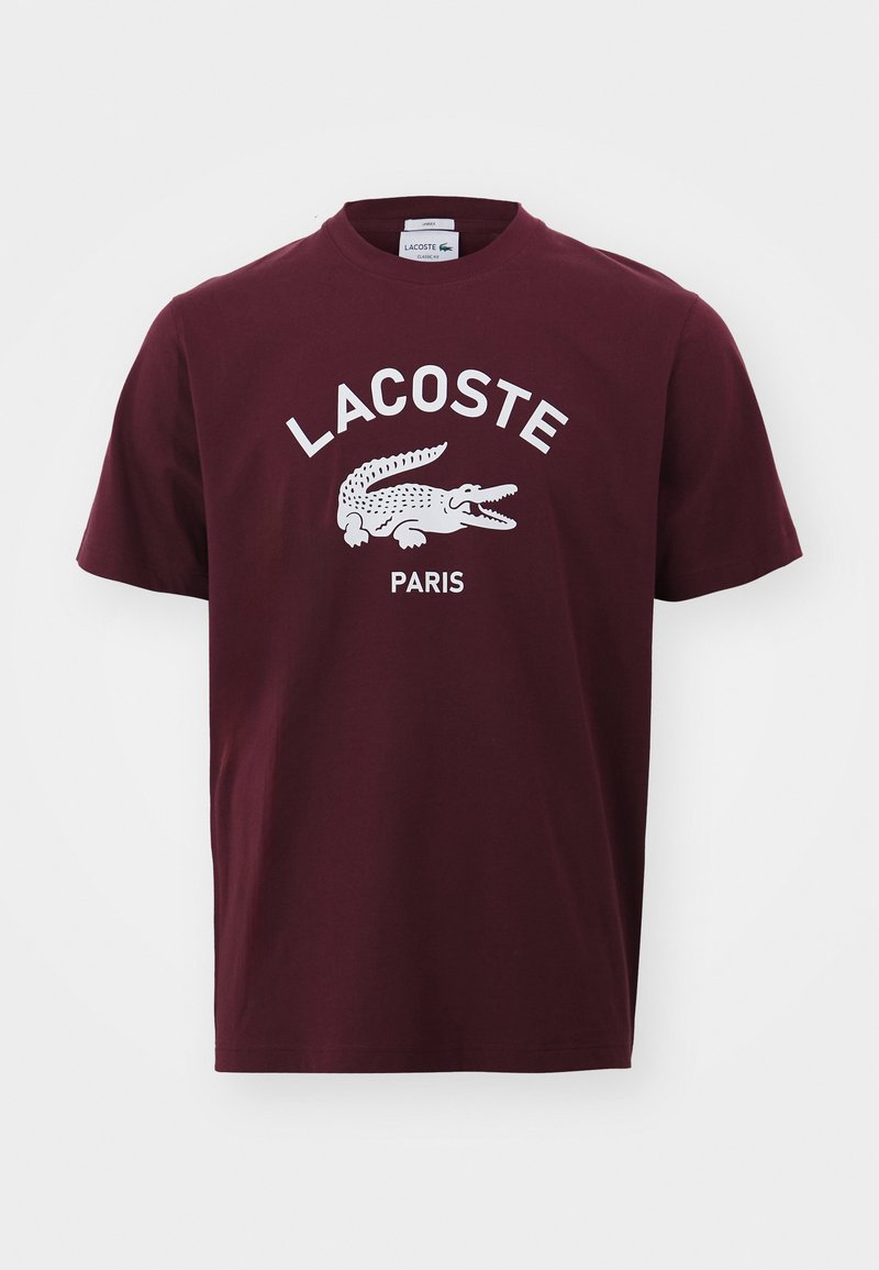 Una camiseta de algodón burdeos con cuello redondo, que presenta un logo de cocodrilo blanco y el texto "LACOSTE PARIS" en una tipografía en negrita. Diseño sencillo.