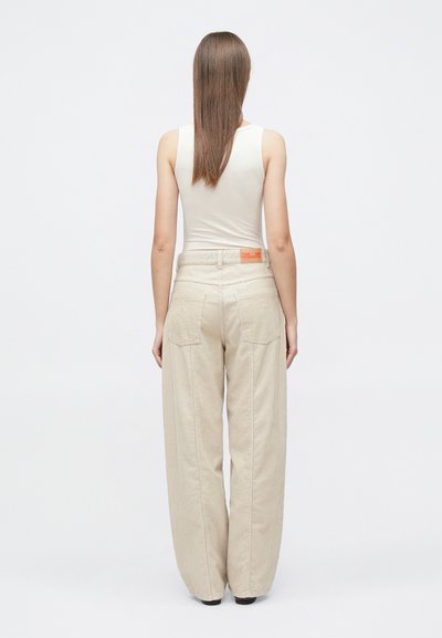 Παλτό παντελόνα σε ανοιχτό μπεζ, κατασκευασμένο από υφή ύφασμα. Διαθέτει δύο τσέπες στο πίσω μέρος και μια μικρή πορτοκαλί ετικέτα στη μέση.