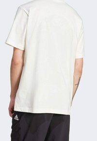 Camiseta de algodón blanca de manga corta, con un sutil diseño texturizado en la parte posterior y un logo de Adidas en el dobladillo inferior izquierdo.