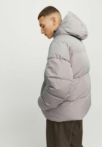 Grå puffjakke med hætte, der har et quiltet design og elastiske manchetter. Stoffet ser glat og let skinnende ud.
