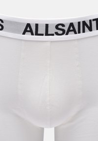 Boxer briefs en coton blanc avec une taille élastique noire portant le texte « ALLSAINTS. » Texture lisse et design ajusté.