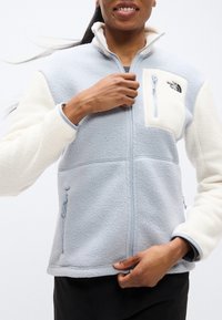 Μπουφάν fleece με ανοιχτό μπλε σώμα, λευκά μανίκια και τσεπάκι στο στήθος με φερμουάρ. Περιλαμβάνει τσεπάκια στο πλάι με φερμουάρ και ελαστικές μανσέτες.