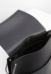 Černá kabelka s texturovanou horní částí a hladkou dolní částí. Obsahuje stříbrné kovové doplňky a otevřenou horní část s vnitřní kapsou.