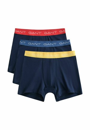Drie marineblauwe herenboxershorts met elastische taillebanden in rood, blauw en geel, elk bedrukt met de tekst "GANT".