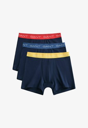 Trois caleçons boxer pour hommes en bleu marine avec des tailles élastiques en rouge, bleu et jaune, chacun estampillé du texte "GANT".