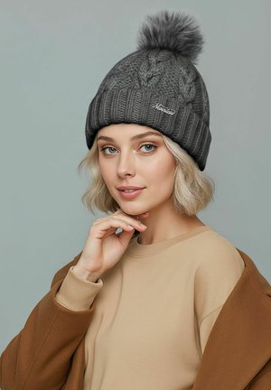 Gray knitted beanie with a pom-pom on top, featuring a cable pattern and a branded accent. Worn over a beige sweatshirt.