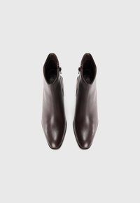 Bottines en cuir marron avec un design à bout pointu, texture lisse et une fermeture éclair sur le côté. Silhouette élégante et structurée.