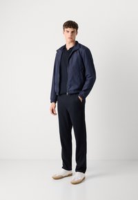 Navy blue lightweight jacket with a zippered front, elastic cuffs and waistband, paired with black trousers and white sneakers.