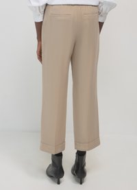 Beige maßgeschneiderte Hose mit geradem Bein, Seitentaschen und krempelbarem Saum, kombiniert mit schwarzen Stiefeletten.