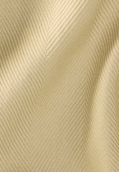 Μπεζ ύφασμα με σχέδιο ύφανσης ψαροκόκκαλο, που εμφανίζει διαγώνιες ραβδώσεις και απαλές πτυχές που δημιουργούν σκιές και υφή.