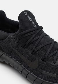 Czarne buty biegowe Nike Free z siateczkową cholewką, plecioną fakturą, czarnymi sznurowadłami, gumową podeszwą i subtelnym logo na języku.