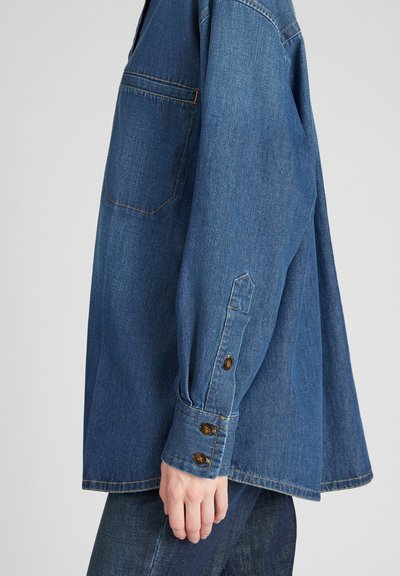 Donkerblauwe denim shirt met een enkele borstzak, knoopmanchetten, zichtbare stitching en een losse pasvorm. Getextureerde stof.