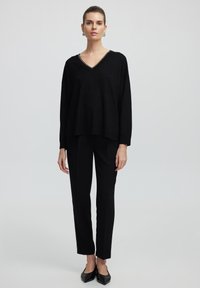 Pull en tricot noir avec un col en V et des bords blancs, associé à un pantalon noir ajusté et des ballerines noires. Style simple, coupe décontractée et texture douce.