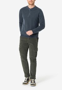 Marineblauwe langerhals T-shirt met drie knopen, gecombineerd met olijfgroene cargobroek met meerdere zakken en zwarte hoge sneakers.