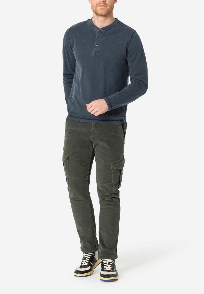 Marineblauwe langerhals T-shirt met drie knopen, gecombineerd met olijfgroene cargobroek met meerdere zakken en zwarte hoge sneakers.