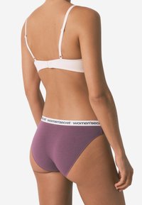 Lila Baumwollunterhosen mit einem weißen, gebrandeten Bund und verstellbaren rosa Trägern auf einem BH, die eine glatte Textur und eine enganliegende Passform zeigen.