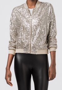 Silberne Pailletten-Bomberjacke mit gerippten Bündchen und Kragen. Verfügt über einen Reißverschluss vorne und eine strukturierte Oberfläche. Tragen Sie sie über schwarzen Leggings.