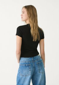 Zwarte korte mouwen aansluitend topje gecombineerd met lichtblauwe, loszittende spijkerbroek met achterzakken. Haar in losse golven gestyled.
