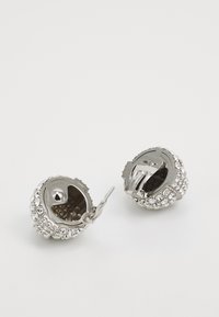 Hõbedased kõrvarõngad ümmarguse disainiga, millel on kaunistuseks selged rhinestones. Sulgemine on klambriga stiilis. Tekstuuriga metallviimistlus.