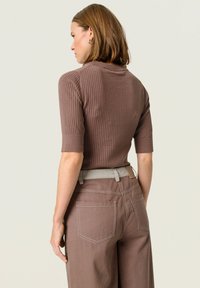 Brown ribbed short-sleeve sweater with a high neckline, paired with beige belted trousers, featuring back pockets and a relaxed fit.