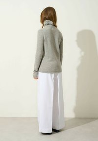 Maglione attillato color grigio chiaro con colletto a lupetto realizzato in un materiale morbido, abbinato a pantaloni bianchi a gamba larga, mostrato di spalle su uno sfondo neutro.