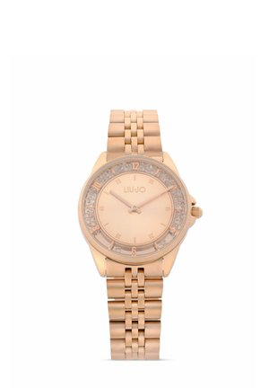 Orologio da polso in oro rosa con cinturino metallico a maglie, dettagli in cristallo attorno al quadrante, e indici e lancette semplici.