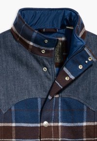 Flannel and denim jacket in blue and brown with a checked pattern. Features a high collar, snap buttons, and a contrasting inner lining.